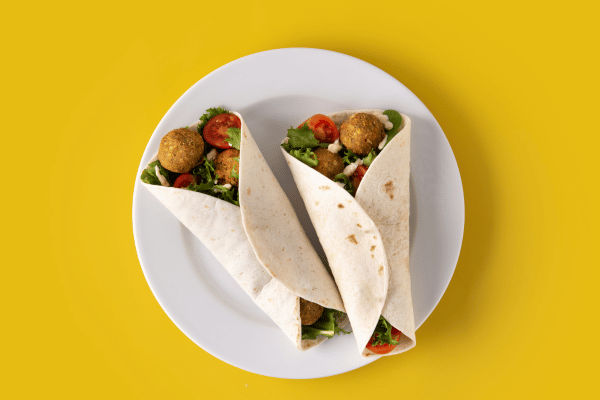 Trader Joe's Cauliflower Thins: Healthy Snack Hacks 11 Hummus and veggie wrap on a plate with a yellow background.