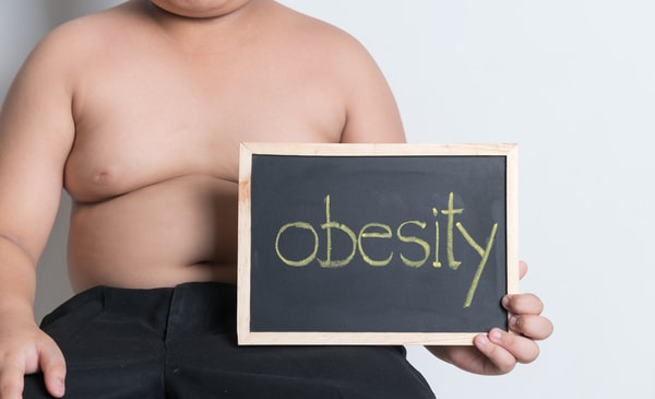 Signs of Gaining Muscle and Losing Fat: Quick and Easy Tips 3 A child holding a blackboard with the word 'obesity' written on it, highlighting the issue of childhood obesity