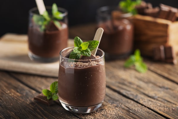 A glass of creamy chocolate mousse garnished with a sprig of mint and a wooden spoon