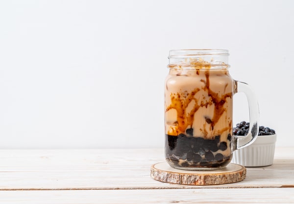 Mason Jar Cold Brew Recipe 101: A Refreshing Beverage Option 5 A mason jar filled with brown sugar boba milk tea, topped with caramel drizzle, sits on a wooden coaster next to a small bowl of boba pearls