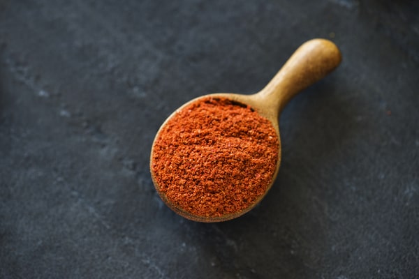A wooden spoon filled with vibrant red chili powder is placed on a dark grey surface
