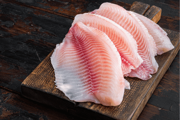 Keto Fish Tacos: The Ultimate Low Carb Recipe and Tips 6 White tilapia fish fillet cuts on dark wooden background.