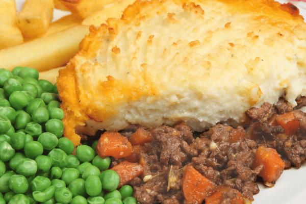Keto Shepherd's Pie Recipe: Quick and Low-Carb Comfort Food 10 A plate holds a hearty serving of shepherd's pie, accompanied by crispy chips and bright green peas.