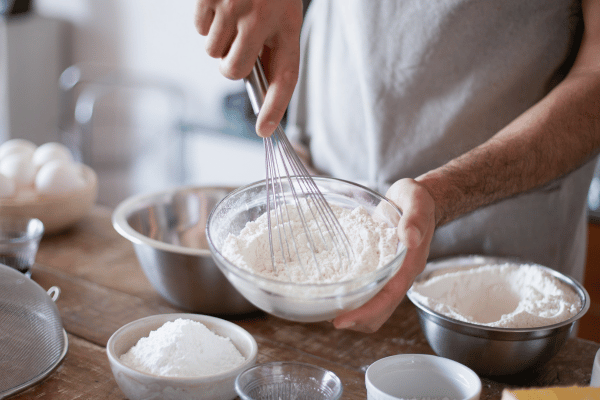 Carb Free Bread Recipe: A Simple Guide for Beginners 5 A person whisking eggs in a bowl, preparing a low-carb bread recipe. Nearby, almond flour, psyllium husk, and baking powder are set out, ready to be mixed.