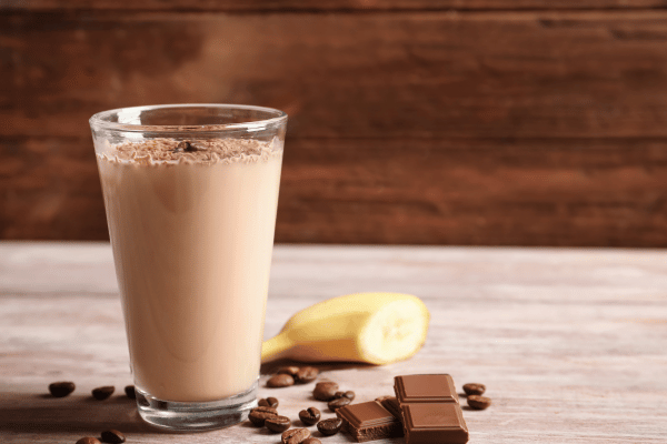 How Low Carb Protein Shakes Can Boost Your Fitness Goals 5 A glass of low carb protein shake sits on a table, with a banana and some pieces of chocolate placed beside it.
