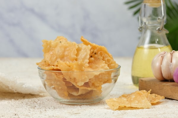 Keto CVS Essentials: Must-Have Products for Your Diet 6 A glass bowl filled with crispy fried dumpling chips, placed on a textured surface with garlic and a bottle of oil in the background
