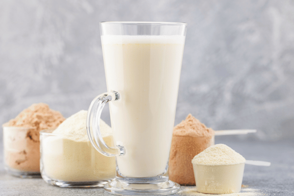 How Low Carb Protein Shakes Can Boost Your Fitness Goals 7 A glass of white low carb protein shake is displayed, with various protein shake powders arranged on the side.