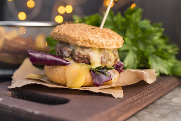 Five Guys Keto: Top Picks for a Low-Carb Fast Food Fix 9 A little bacon cheeseburger with melted cheese and fresh greens served on a crispy bun, with a festive background of blurred lights and parsley