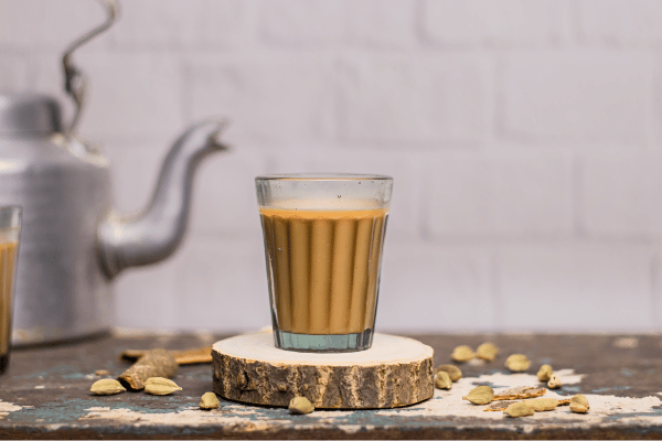 Dutch Bros Chai Drinks vs Competitors: Who Wins? 2 A khaki chai drink in a clear glass, with a gray kettle softly blurred in the background.