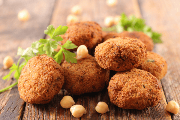 Is Falafel Keto Friendly? How to Make Low-Carb Versions 11 A stack of crispy, golden-brown falafel on a rustic wooden table, surrounded by a scattering of nuts, herbs, and spices.