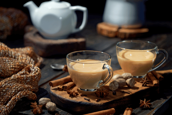 Dutch Bros Chai Drinks vs Competitors: Who Wins? 4 Two clear cups of hot chai on a wooden board, with a white teapot in the background.