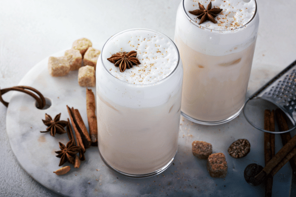 Dutch Bros Chai Drinks vs Competitors: Who Wins? 12 Two iced spiced lattes topped with frothy cream and star anise, surrounded by sugar cubes and spices.