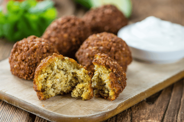 Is Falafel Keto Friendly? How to Make Low-Carb Versions 4 Crispy, golden brown keto falafel on a rustic wooden plate, with one falafel sliced open by hand, revealing the tender inside.