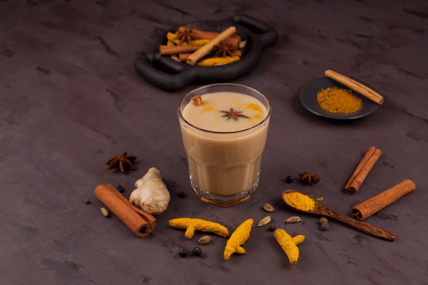 Dutch Bros Chai Drinks vs Competitors: Who Wins? 8 A clear glass of chai sits with a spoon of flavorings and a two-handled container of spices nearby.