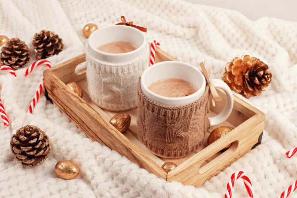 Keto Hot Cocoa: How to Make the Perfect Low-Carb Cup 8 Two festive mugs of keto hot cocoa, each adorned with Christmas decorations, sitting on a rustic wooden tray.