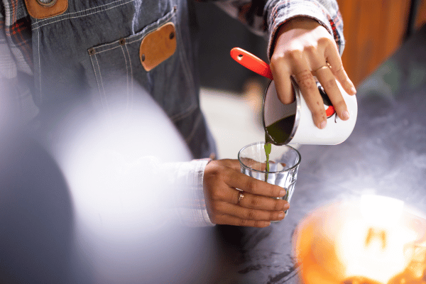 Dutch Bros Chai Drinks vs Competitors: Who Wins? 9 A person pours a vibrant green chai drink from one cup into a clear glass, creating a refreshing scene.
