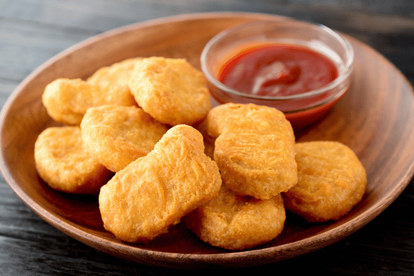 Chicken McNuggets Carbs: A Guide for Low-Carb Dieters 7 Crispy chicken nuggets served on a beautifully textured brown wooden plate, with a side of vibrant dipping sauce for added flavor.