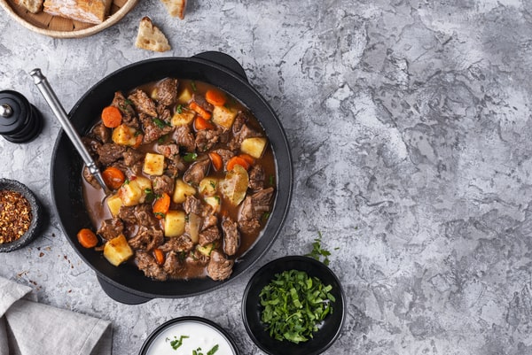 Keto Pot Roast: A Hearty and Healthy Meal Option! 2 A hearty pot roast with tender chunks of beef, potatoes, carrots, and herbs in a cast iron pot, surrounded by fresh parsley, bread, and seasonings