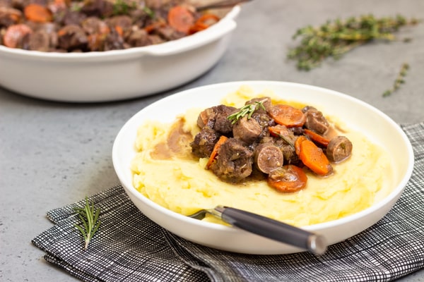 Keto Pot Roast: A Hearty and Healthy Meal Option! 4 A plate of creamy mashed potatoes topped with tender beef pot roast, carrots, and mushrooms, garnished with fresh herbs, set on a gray table with a patterned cloth