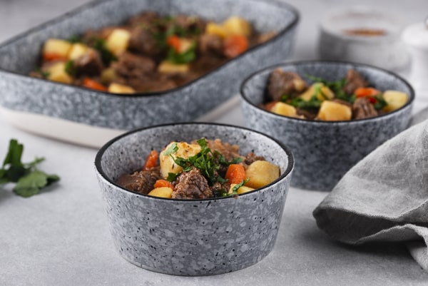 Keto Pot Roast: A Hearty and Healthy Meal Option! 6 Two bowls filled with hearty pot roast beef, potatoes, and carrots, garnished with fresh parsley, were placed in front of a matching serving dish filled with more stew on a light gray tabletop