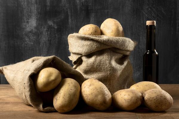 Are Potatoes Keto? Find Out the Surprising Facts 3 Whole raw potatoes spill from burlap sacks onto a wooden surface beside a dark glass bottle