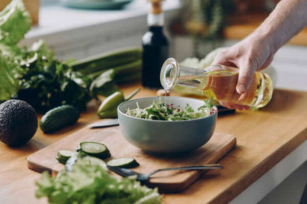Keto Caesar Dressing That's Creamy, Tangy, and Easy 7 Pouring olive oil from a bottle into a salad with cucumber and lettuce