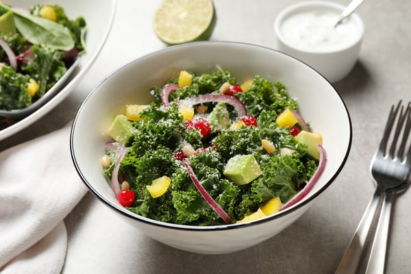 10 Low Carb Salads Perfect for Summer Picnics 7 A low-carb kale salad with avocado, yellow bell pepper, red onion, and berries, served in a white bowl with a creamy dressing on the side