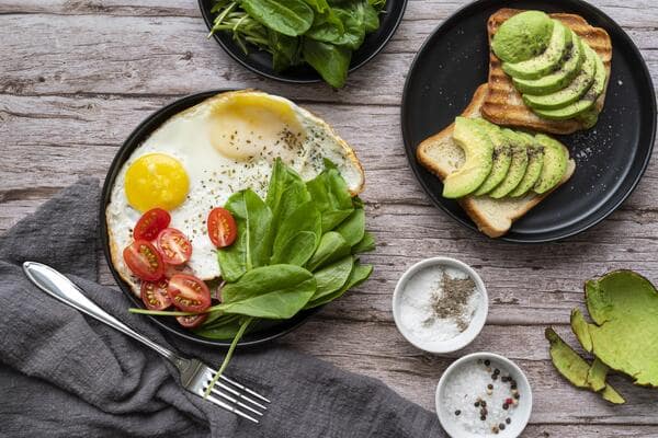 16 Tasty Keto Brunch Ideas: Sweet and Savory Combos 2 A healthy keto brunch with fried eggs, fresh spinach, cherry tomatoes, and avocado on toast, served on a wooden table