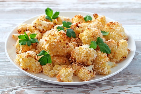 Cauliflower Bake: Deliciously Cheesy and Healthy Recipe 2 A plate of golden-baked cauliflower florets, garnished with fresh parsley, sits on a wooden table