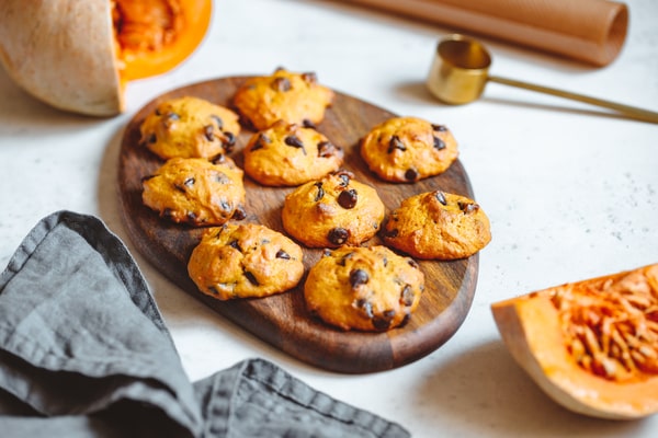 Keto Pumpkin Cookies: Perfect for Holiday Baking Ideas 2 A wooden board filled with freshly baked keto pumpkin cookies with chocolate chips, surrounded by pumpkin pieces and baking tools