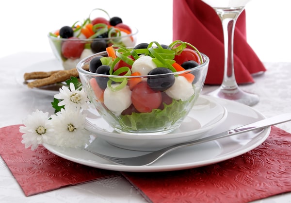 Easy Red White and Blue Salad Recipe for Your BBQ 2 A glass bowl of red white and blue salad with lettuce, cherry tomatoes, mozzarella balls, blueberries, and sliced peppers, served on a white plate with a red napkin