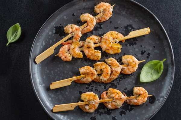 21 Keto Chinese Recipes: Enjoy Takeout Without the Carbs 11 A top-down view of four shrimp skewers resting on a dark, textured plate, garnished with basil leaves.