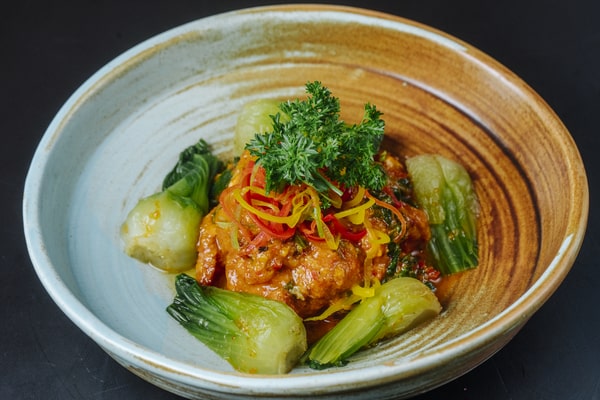 21 Keto Chinese Recipes: Enjoy Takeout Without the Carbs 12 A close-up of a bowl filled with saucy chicken and bok choy, garnished with thinly sliced red and yellow peppers and a sprig of parsley.