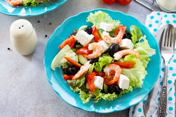 Easy Red White and Blue Salad Recipe for Your BBQ 3 A blue plate of red white and blue salad with shrimp, feta cheese, black olives, lettuce, cucumbers, and red bell peppers