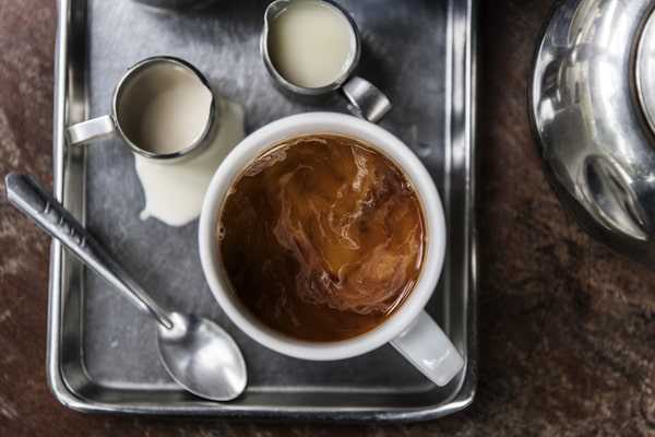 How Much Caffeine in Decaf Espresso: Brewing Insights 3 A cup of decaf espresso with milk swirling on top, served on a tray with creamers and a spoon