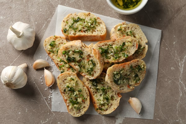 Frozen Garlic Bread in Air Fryer: Ready in 5 Minutes! 4 Slices of garlic bread topped with fresh herbs, placed on parchment paper with garlic cloves nearby