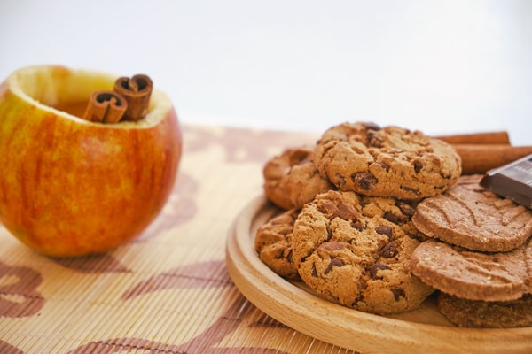 Keto Pumpkin Cookies: Perfect for Holiday Baking Ideas 4 A wooden plate filled with cookies and chocolate pieces beside an apple cup holding cinnamon sticks