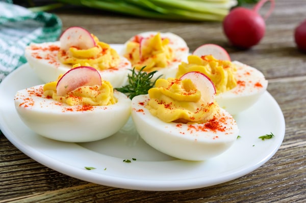 Keto Meal Prep Guide: 19 Quick Ideas and Time-Saving Hacks 4 A plate of deviled eggs topped with paprika and sliced radishes served on a wooden table