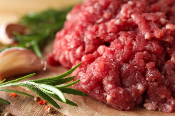 Calories in Ground Beef: Health Facts You Should Know 4 A close-up of raw ground beef on parchment paper, surrounded by fresh rosemary, garlic cloves, and pepper flakes