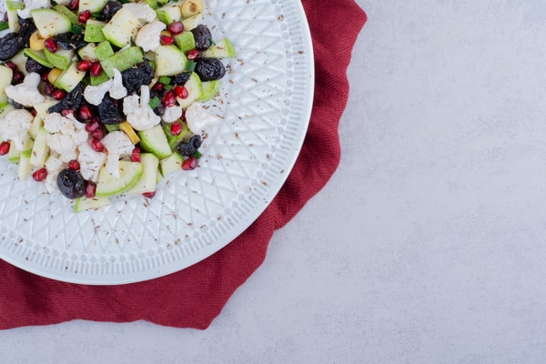 Easy Red White and Blue Salad Recipe for Your BBQ 4 A white plate of red white and blue salad with cauliflower, green apples, black olives, pomegranate seeds, and nuts