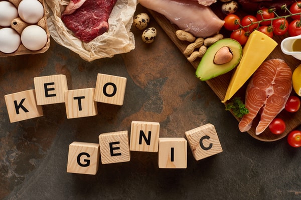 3 Day Keto Diet: Simple Steps to Jumpstart Ketosis 5 A flat lay of keto-friendly foods such as eggs, meat, fish, avocado, cheese, nuts, and tomatoes with wooden blocks spelling "KETOGENIC"