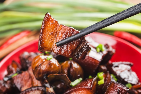 21 Keto Chinese Recipes: Enjoy Takeout Without the Carbs 5 A single piece of glossy, barbeque pork is lifted with black chopsticks from a red plate of food.