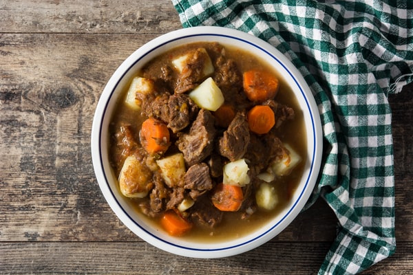 Keto Meal Prep Guide: 19 Quick Ideas and Time-Saving Hacks 5 A bowl of beef stew with chunks of meat, carrots, and potatoes on a wooden table next to a green checkered cloth