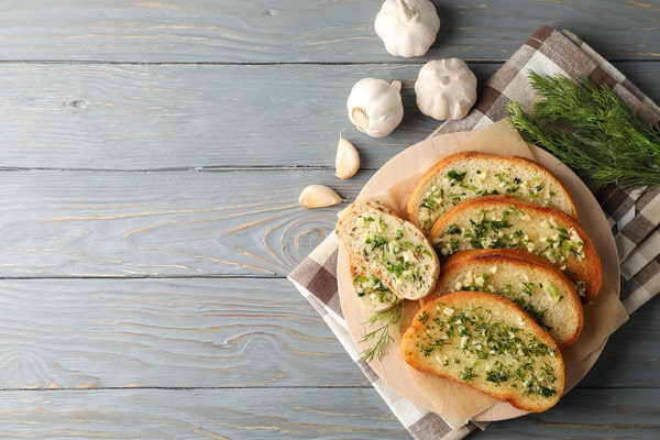 Frozen Garlic Bread in Air Fryer: Ready in 5 Minutes! 5 Slices of garlic bread topped with fresh herbs, arranged on a wooden board beside garlic cloves and dill