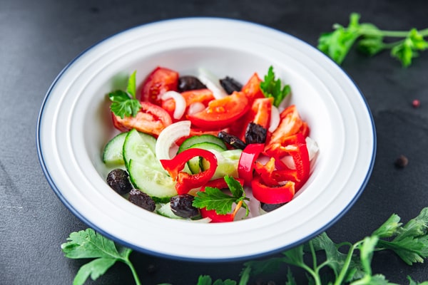 Easy Red White and Blue Salad Recipe for Your BBQ 5 A white bowl of red white and blue salad with cucumbers, tomatoes, red peppers, onions, black olives, and fresh parsley