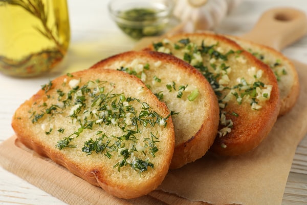 Frozen Garlic Bread in Air Fryer: Ready in 5 Minutes! 6 Slices of toasted garlic bread topped with chopped herbs, placed on parchment paper with olive oil and garlic in the background