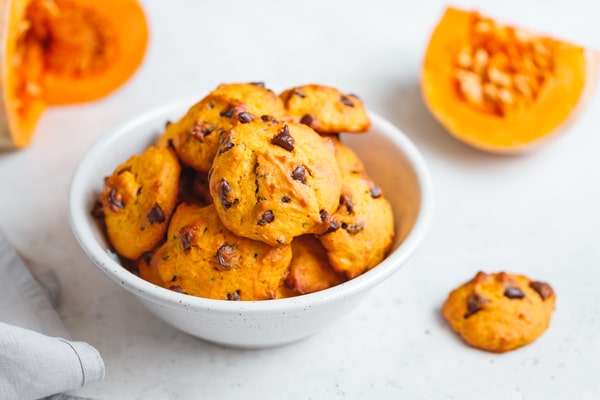 Keto Pumpkin Cookies: Perfect for Holiday Baking Ideas 6 A white bowl filled with keto pumpkin cookies with chocolate chips, placed beside fresh pumpkin halves