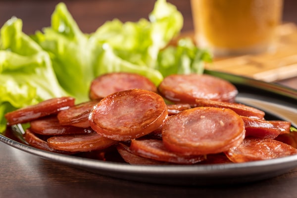 Keto Meal Prep Guide: 19 Quick Ideas and Time-Saving Hacks 6 A plate of sliced cooked pepperoni with lettuce in the background
