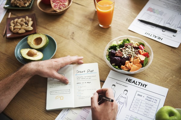 3 Day Keto Diet: Simple Steps to Jumpstart Ketosis 7 A person writing in a diet journal at a table with healthy foods, a salad bowl, and nutrition papers