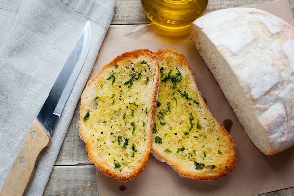 Frozen Garlic Bread in Air Fryer: Ready in 5 Minutes! 7 Two slices of garlic bread with herbs, placed next to a loaf of bread, a knife, and a bottle of olive oil